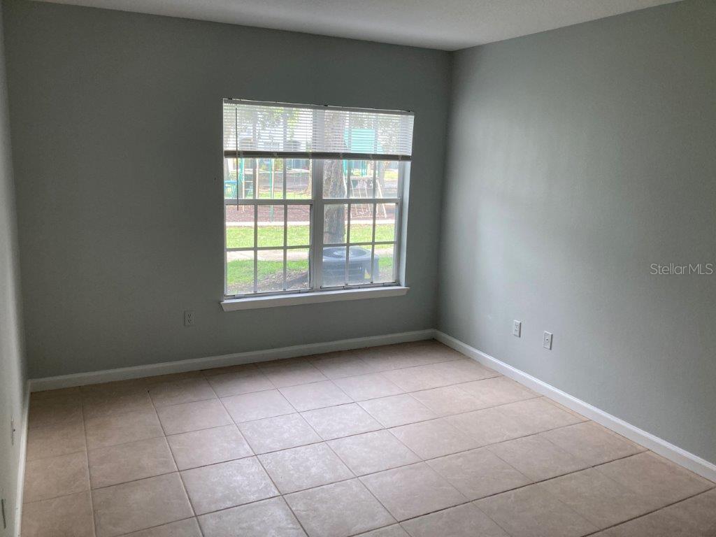 An empty room features light gray walls, tile flooring, and a window overlooking a playground — 4352 S KIRKMAN ROAD UNIT 1211, ORLANDO, FL
