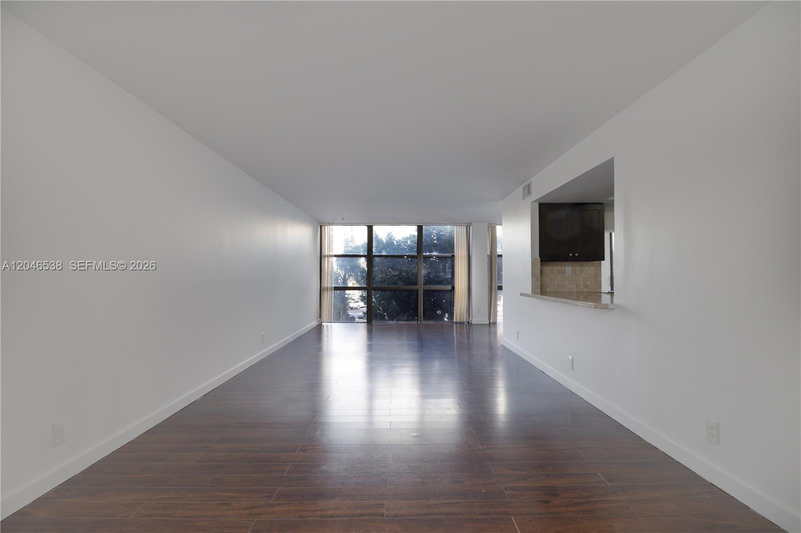 An empty living room features dark wood flooring, white walls, and a large window wall — 1000 Parkview Dr # 302, Hallandale Beach FL 33009, HALLANDALE BEACH, FL