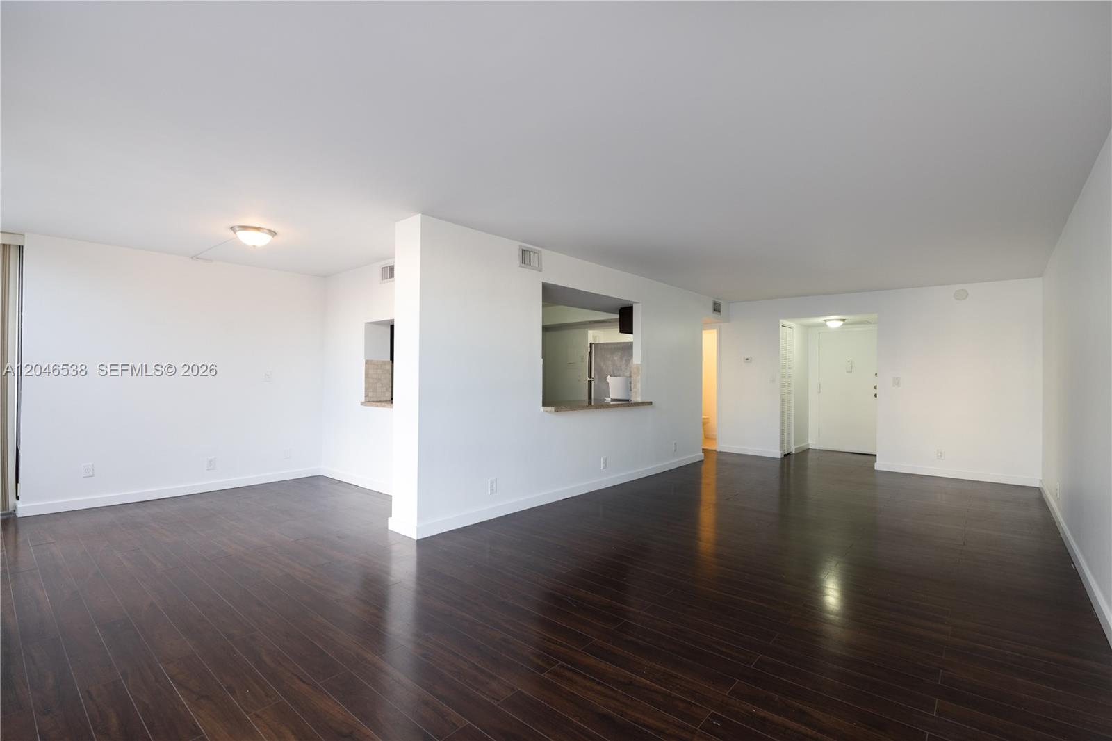 An empty living area features dark wood-look flooring, white walls, and a kitchen pass-through window — 1000 Parkview Dr # 302, Hallandale Beach FL 33009, HALLANDALE BEACH, FL