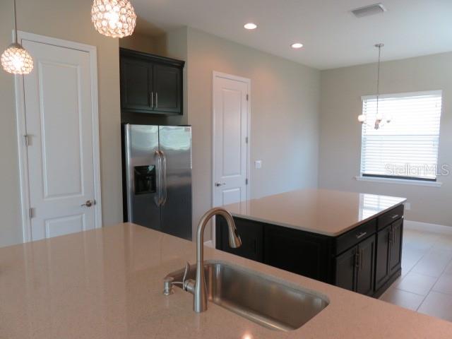 A kitchen features a large island with a sink, stainless steel refrigerator, and dark cabinetry — 5827 TITLE ROW DRIVE, BRADENTON, FL