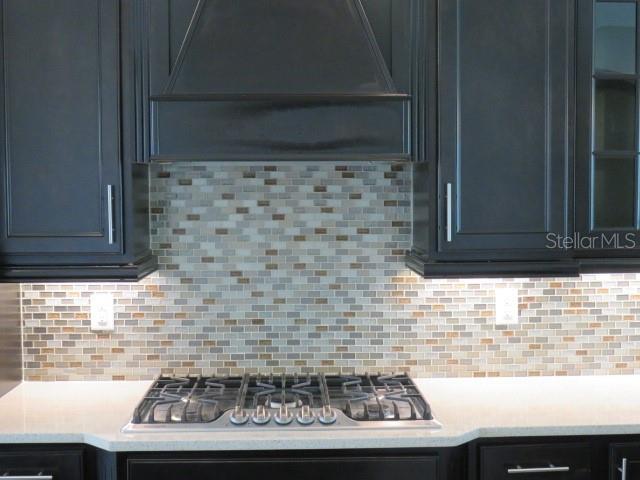 A kitchen features dark cabinets, a gas cooktop, and a multi-colored mosaic tile backsplash — 5827 TITLE ROW DRIVE, BRADENTON, FL