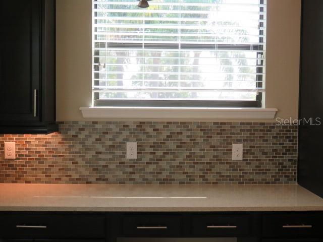 A kitchen features dark cabinets, a light countertop, and a multi-colored glass tile backsplash — 5827 TITLE ROW DRIVE, BRADENTON, FL