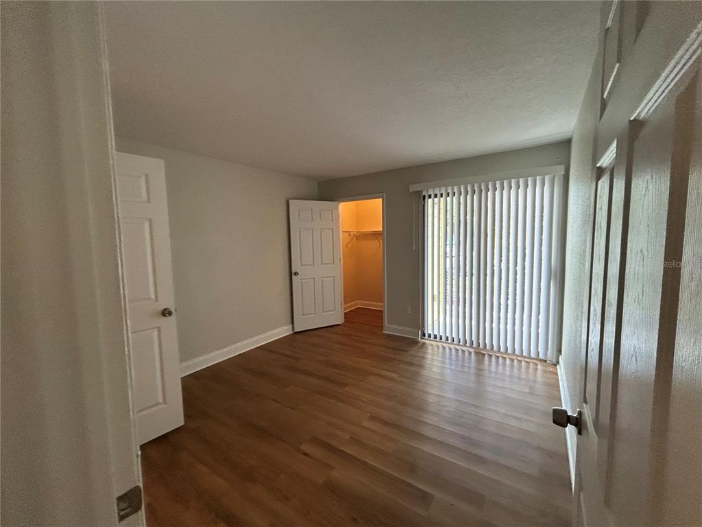 An empty bedroom features wood-look flooring, a walk-in closet, and a sliding glass door — 455 ALT 19 S UNIT 121, PALM HARBOR, FL