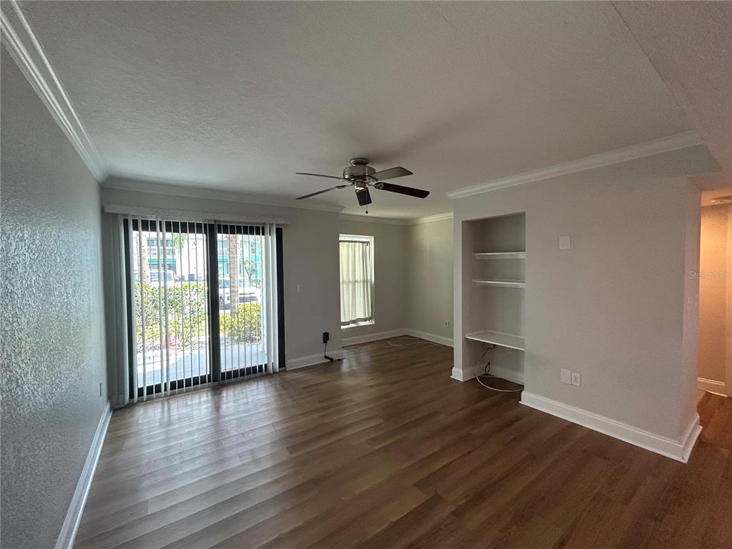 A living room features wood-look flooring, a ceiling fan, sliding glass doors, and built-in shelving — 455 ALT 19 S UNIT 121, PALM HARBOR, FL