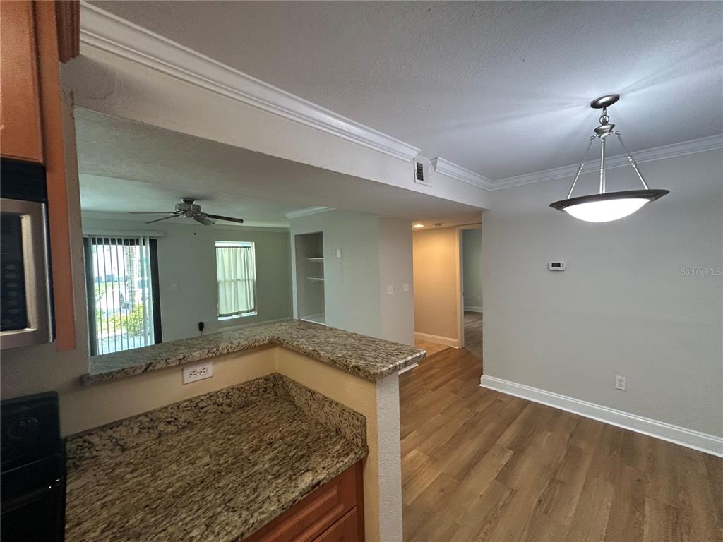 A kitchen with granite countertops overlooks a dining area with wood-look flooring and a chandelier — 455 ALT 19 S UNIT 121, PALM HARBOR, FL