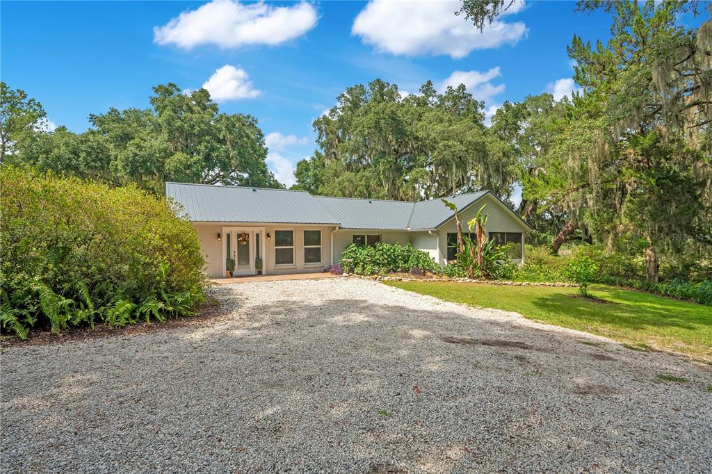 A single-story house with a metal roof and gravel driveway surrounded by mature trees — 41832 CARRIE LANE, ALTOONA, FL