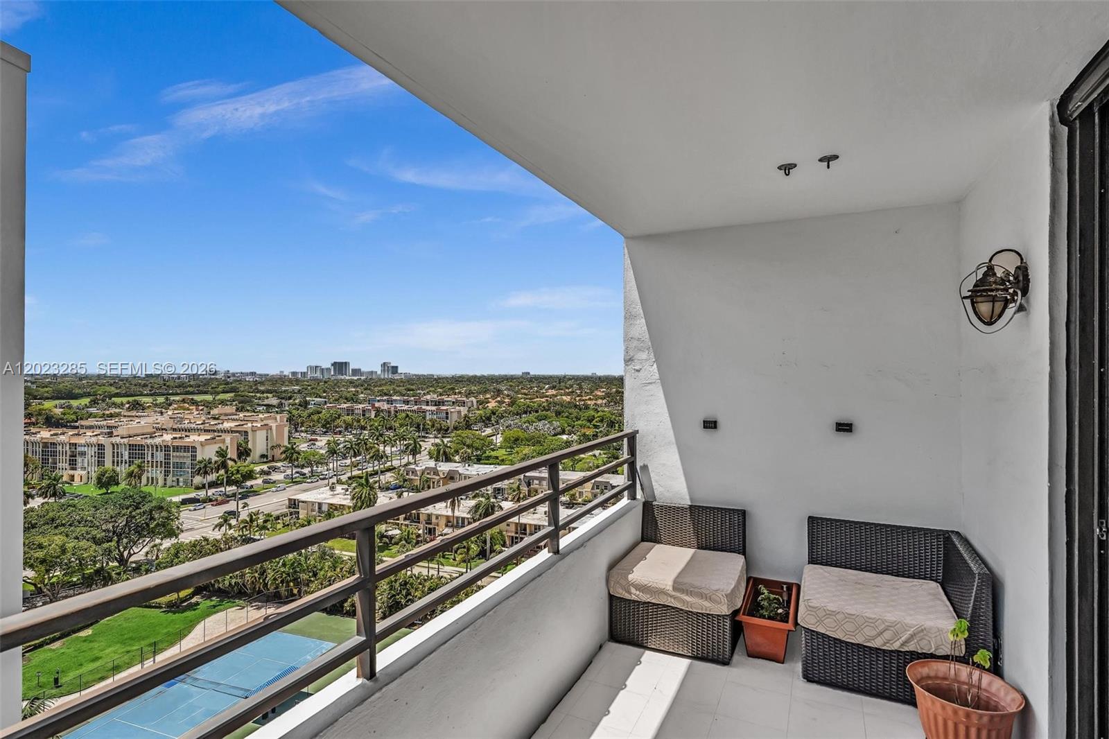 A balcony with wicker seating overlooks a suburban landscape with a tennis court below — 2500 Parkview Dr # 1514, Hallandale Beach FL 33009, HALLANDALE BEACH, FL