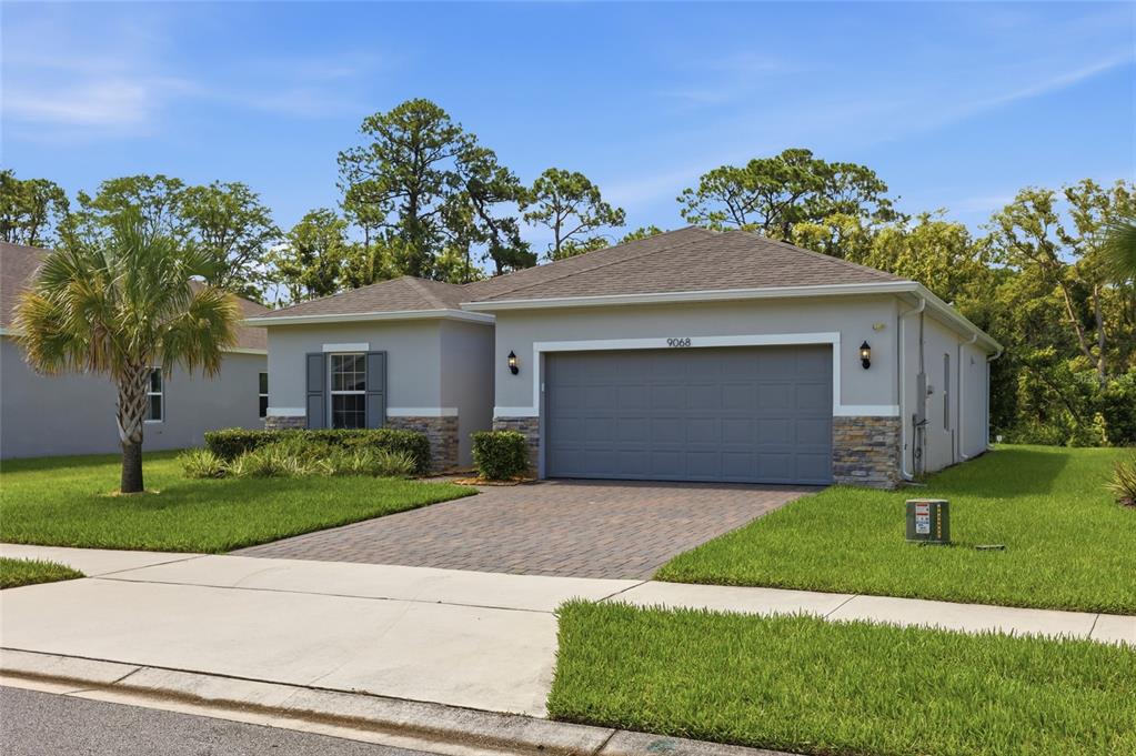 A single-story house with a gray garage, stone accents, and a palm tree in front — 9068 CAPE COD ROAD, DELAND, FL