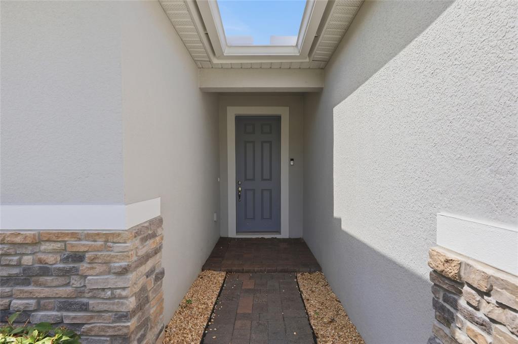 A covered entryway features a blue front door, stone accents, and a skylight above — 9068 CAPE COD ROAD, DELAND, FL