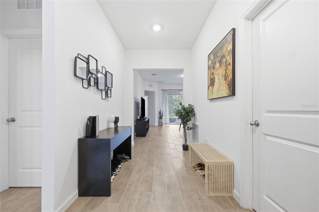 A bright hallway with light wood-look tile flooring leads to an open living area — 9068 CAPE COD ROAD, DELAND, FL