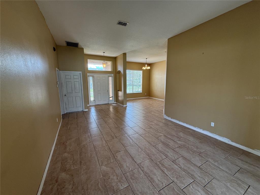 An empty room with tan walls, tile flooring, a front entrance, and a large window — 7101 WHITE TRILLIUM CIRCLE, ORLANDO, FL