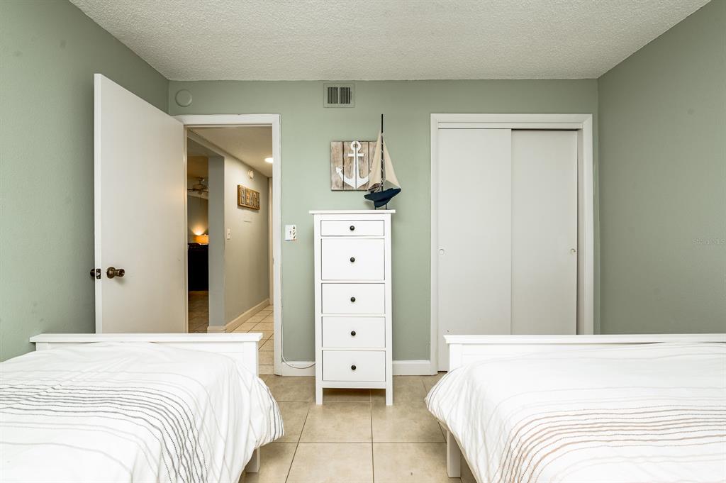 A bedroom features two beds, a white dresser, and a closet against light green walls — 3801 S ATLANTIC AVENUE UNIT 107, NEW SMYRNA BEACH, FL