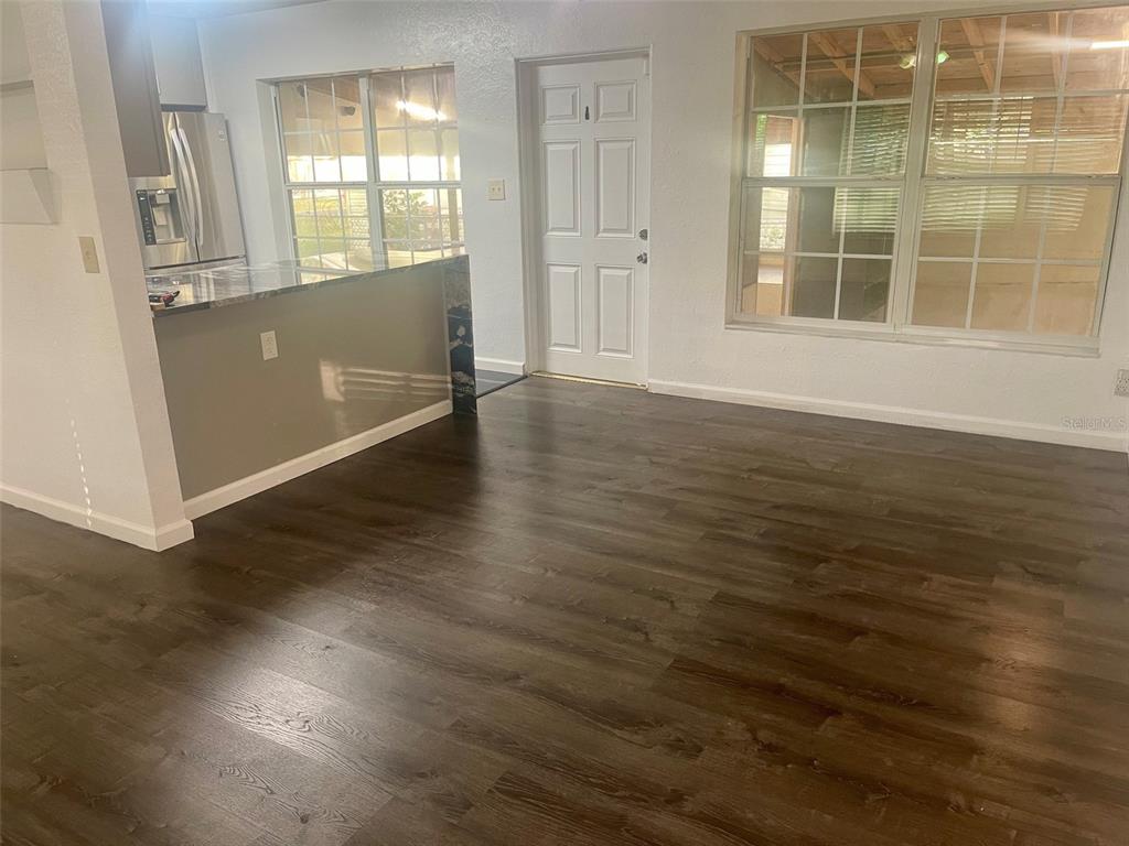 An open-concept room features dark wood-look flooring, a kitchen peninsula, and a white exterior door — 3995 40TH STREET N, ST PETERSBURG, FL