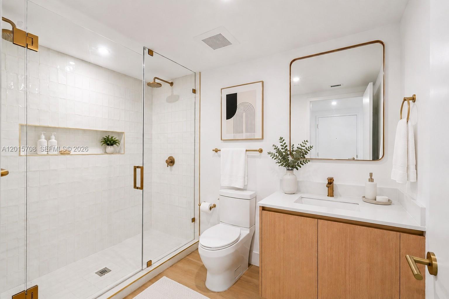 A modern bathroom features a glass-enclosed shower, wood vanity, and gold fixtures — 90 NE 32nd # 313, Miami FL 33137, MIAMI, FL
