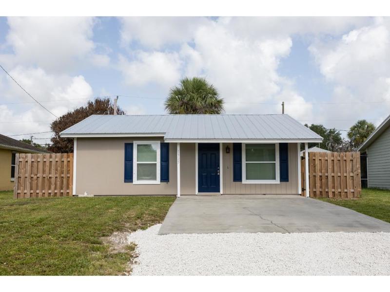 A single-story house with a metal roof, blue shutters, and a concrete driveway — VERO BEACH, FL