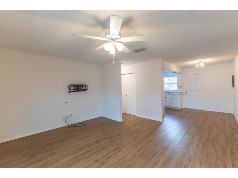 A living room with wood-look flooring, a ceiling fan, and an adjacent kitchen area — VERO BEACH, FL