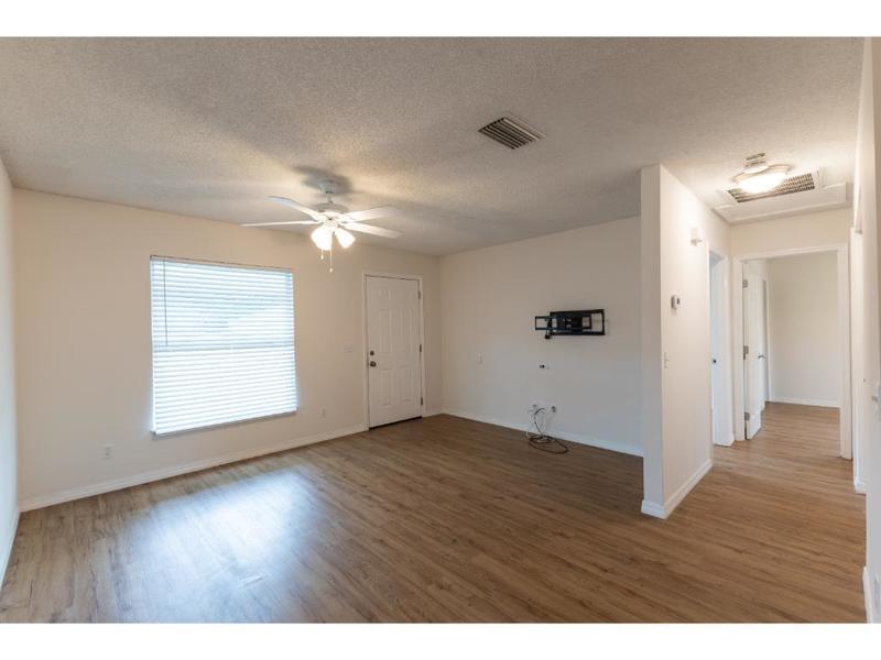 An empty living room features light-colored walls, wood-look flooring, a ceiling fan, and a doorway — VERO BEACH, FL