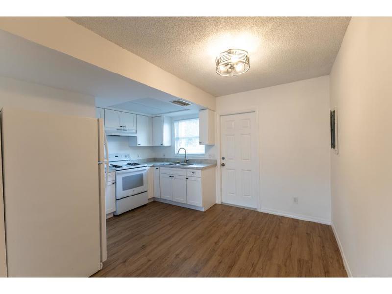 A kitchen with white cabinets, white appliances, and wood-look flooring next to a white door — VERO BEACH, FL