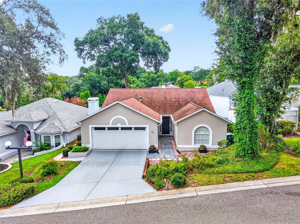 A single-story house with a two-car garage, tan stucco exterior, and a brown shingled roof — 57 TOWNHILL DRIVE, EUSTIS, FL