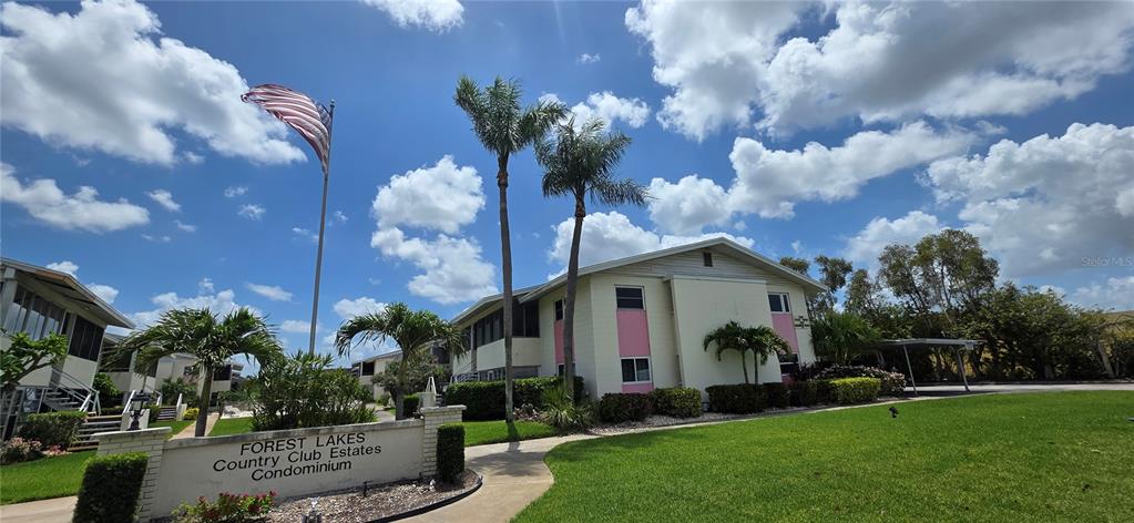 The exterior of a two-story condominium building features a sign, palm trees, and an American flag — 2507 BENEVA ROAD UNIT 5, SARASOTA, FL