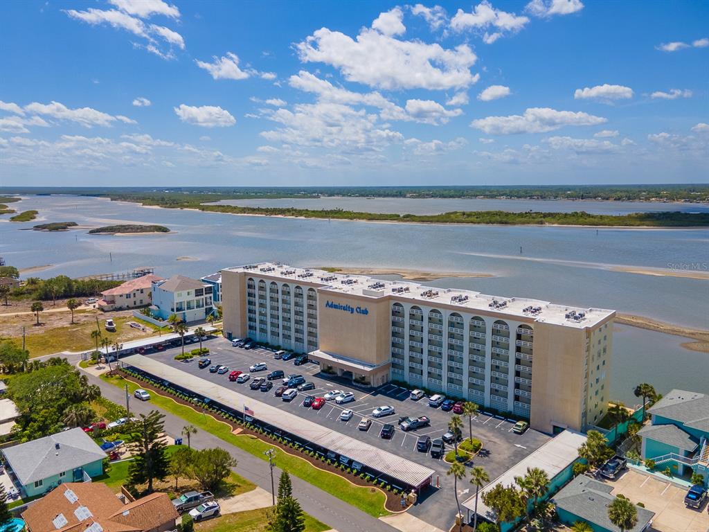 An aerial view shows the Admiralty Club apartment building with a parking lot beside water — 3606 S PENINSULA DRIVE UNIT 703, PORT ORANGE, FL