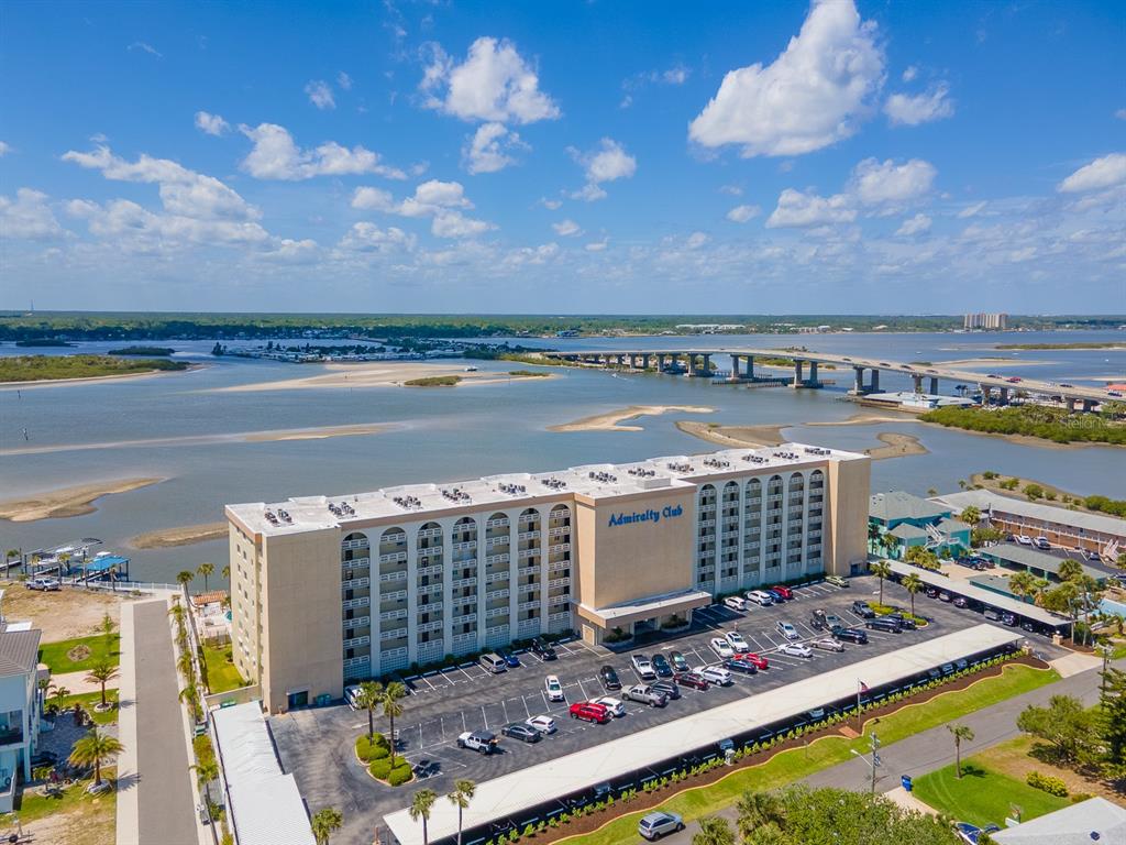 An aerial view shows the Admiralty Club apartment building with a parking lot and bridge — 3606 S PENINSULA DRIVE UNIT 703, PORT ORANGE, FL