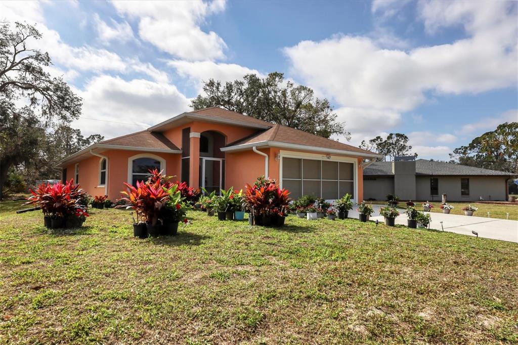 A single-story orange house with a screened-in garage and many potted plants in the yard — 11907 DE LEON DRIVE, NORTH PORT, FL