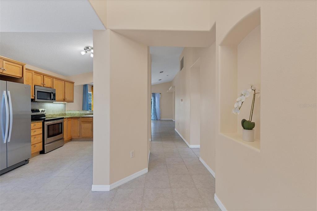 A kitchen with wood cabinets and stainless steel appliances sits beside a tiled hallway niche — 11907 DE LEON DRIVE, NORTH PORT, FL