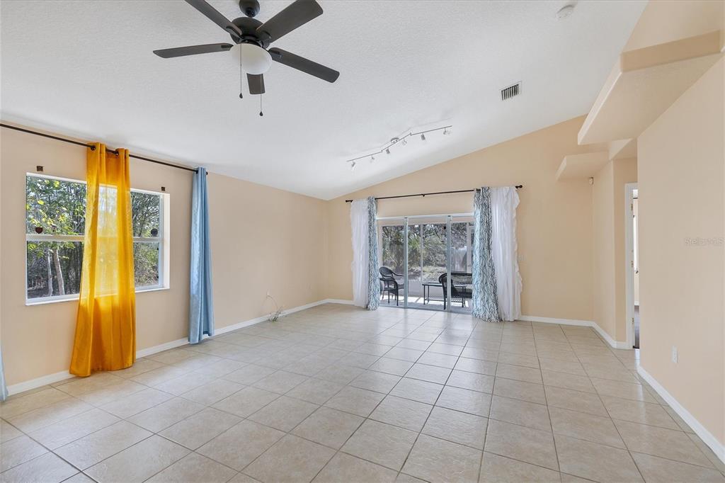 A spacious living room features light tile flooring, a vaulted ceiling, and sliding glass doors — 11907 DE LEON DRIVE, NORTH PORT, FL