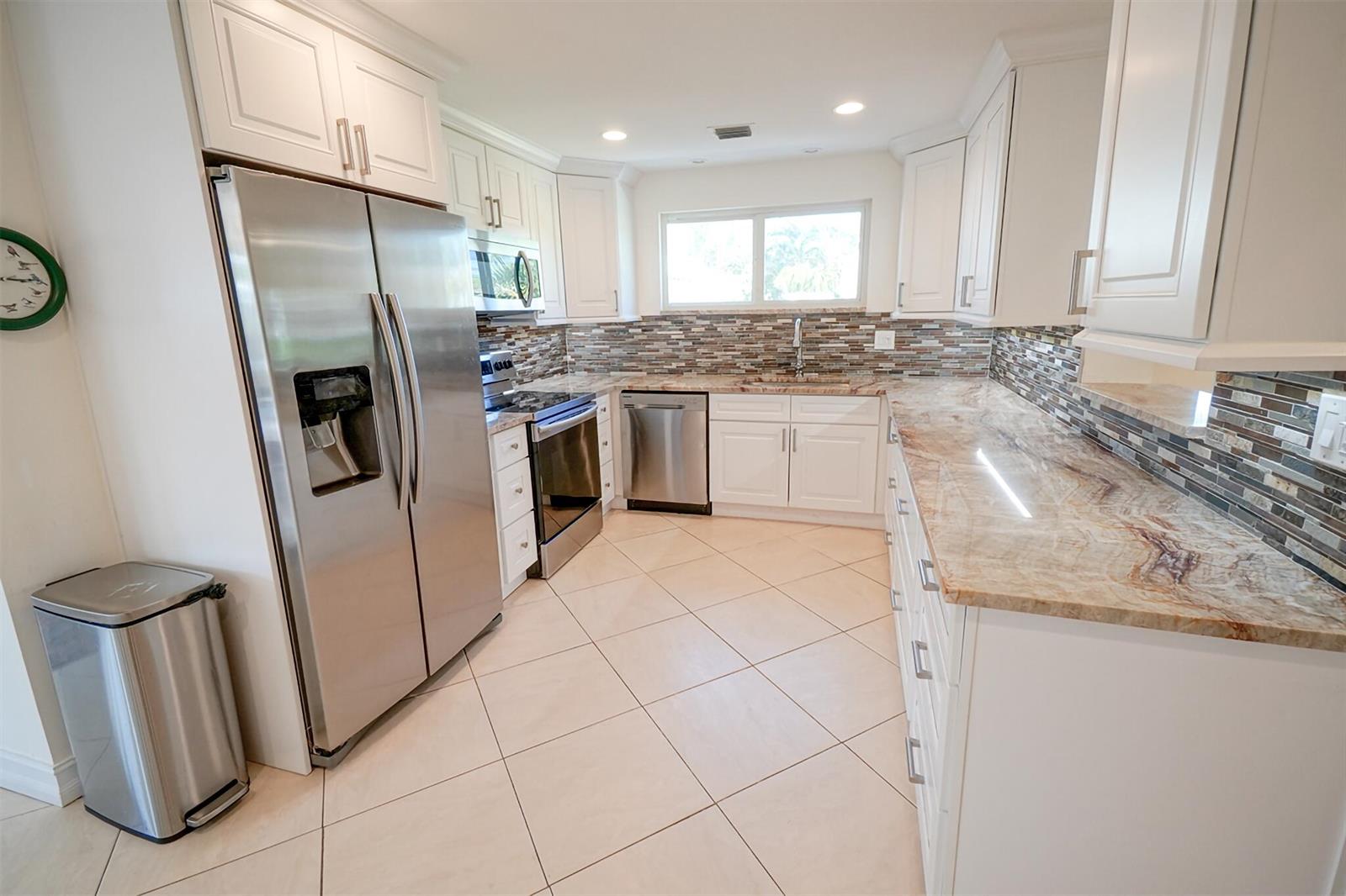 A kitchen features white cabinets, stainless steel appliances, granite countertops, and a tiled backsplash — 3216 Karen Drive, Delray Beach FL 33483, DELRAY BEACH, FL