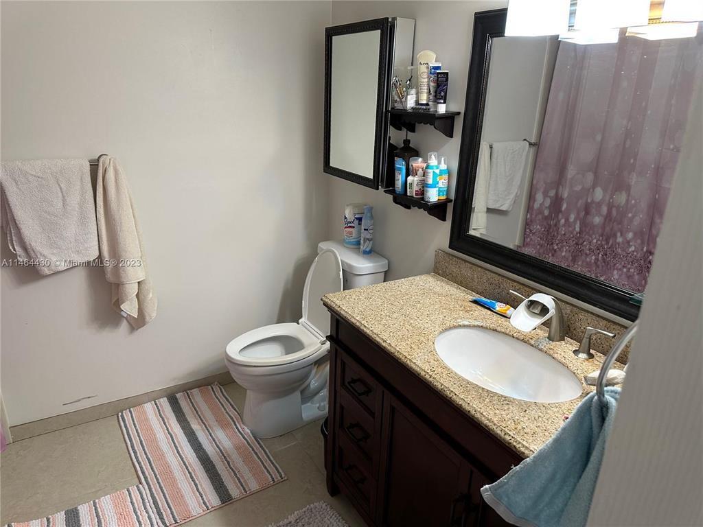 A bathroom features a vanity with a granite countertop, a toilet, and a wall mirror — 200 Leslie Drive # 1128, Hallandale Beach FL 33009, HALLANDALE BEACH, FL
