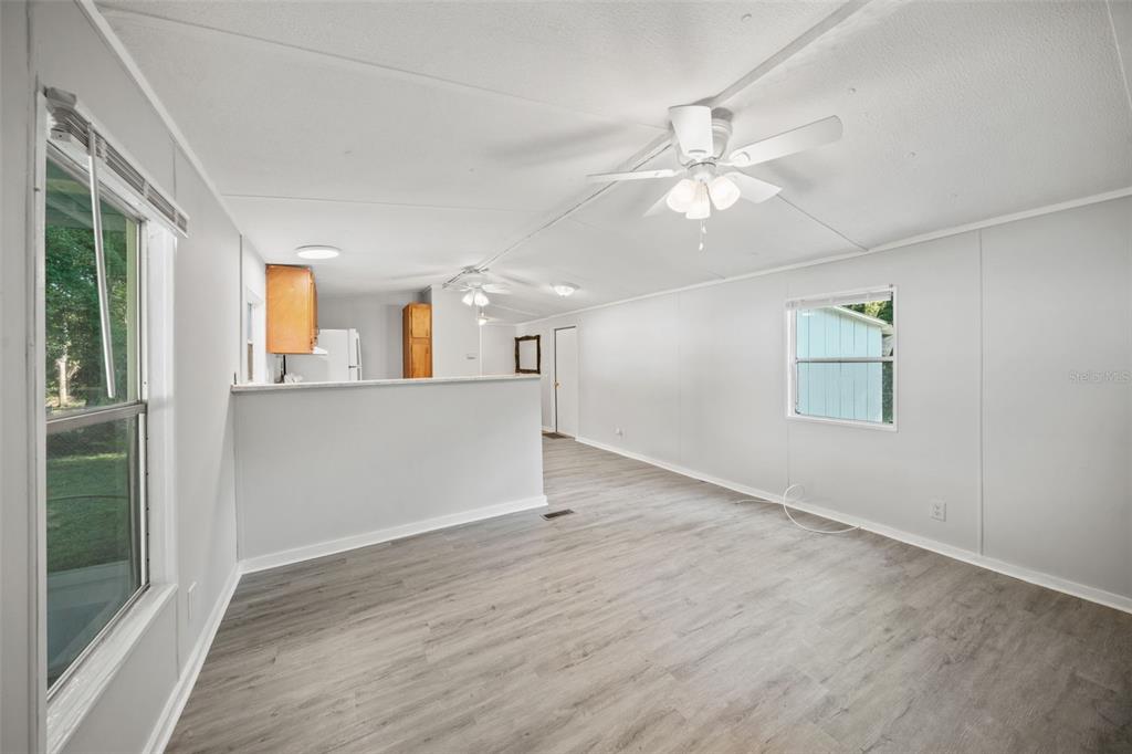 A living room with light gray walls, wood-look flooring, a ceiling fan, and an open kitchen — 1940 CR 428, LAKE PANASOFFKEE, FL