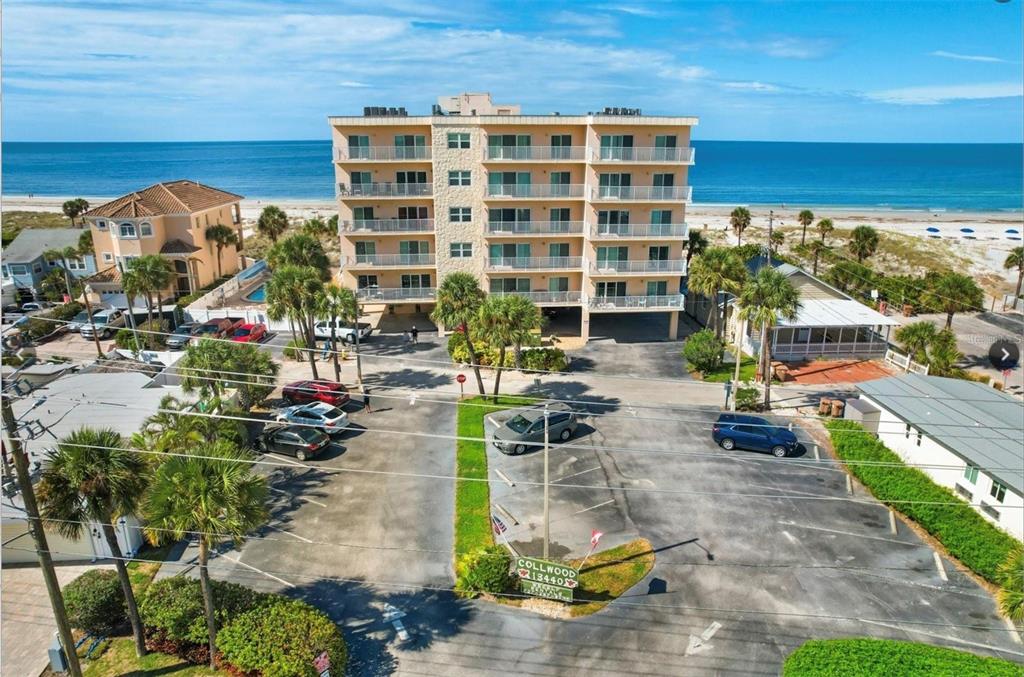 An aerial view of a multi-story beachfront condominium building with a parking lot in front — 13440 GULF BOULEVARD UNIT 202, MADEIRA BEACH, FL