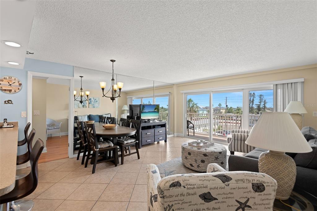 An open-concept living and dining area features tile flooring, mirrored walls, and a balcony view — 13440 GULF BOULEVARD UNIT 202, MADEIRA BEACH, FL