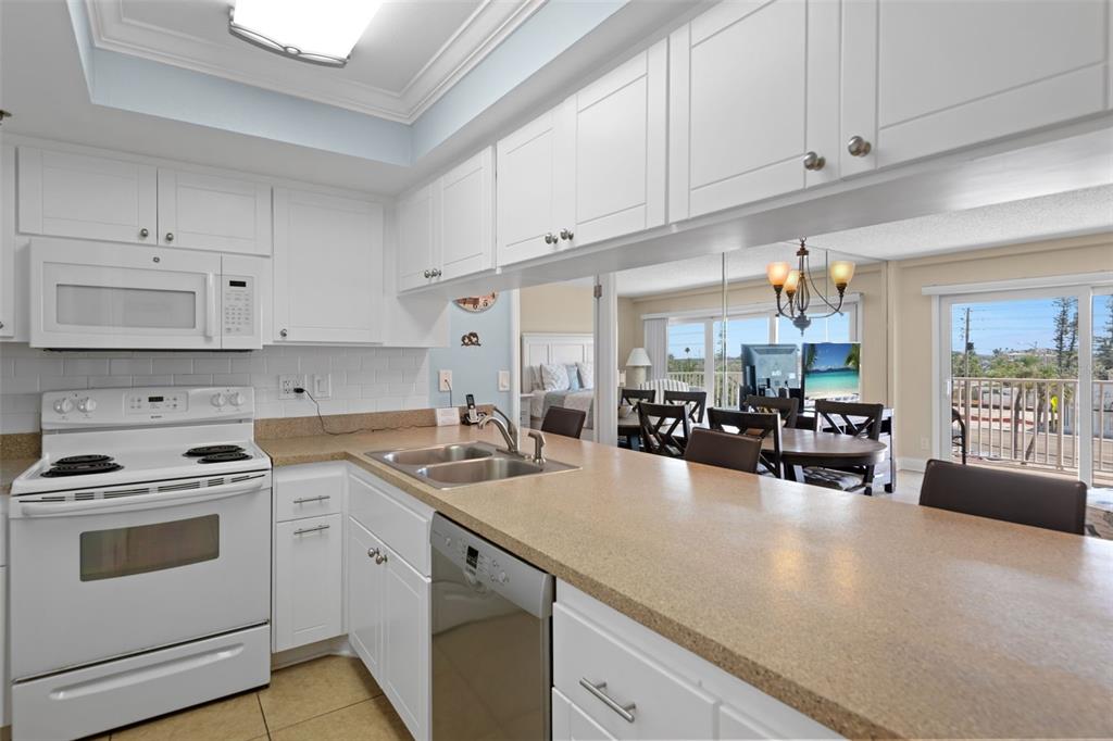 A white kitchen with a breakfast bar overlooks a dining area and a balcony — 13440 GULF BOULEVARD UNIT 202, MADEIRA BEACH, FL