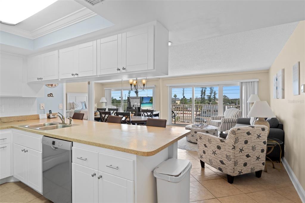 A kitchen with white cabinets and a breakfast bar overlooks a living and dining area — 13440 GULF BOULEVARD UNIT 202, MADEIRA BEACH, FL