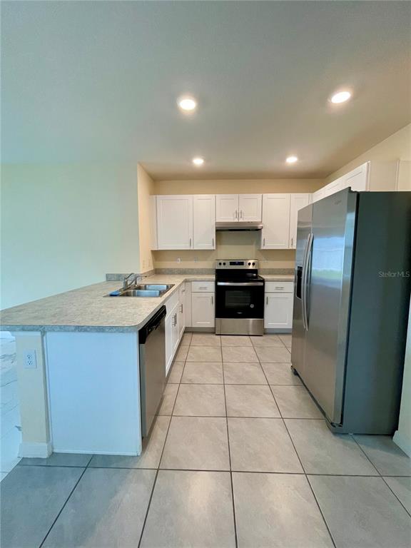 A kitchen features white cabinets, stainless steel appliances, and a light-colored countertop — 1617 HEART BAR ROAD, KISSIMMEE, FL