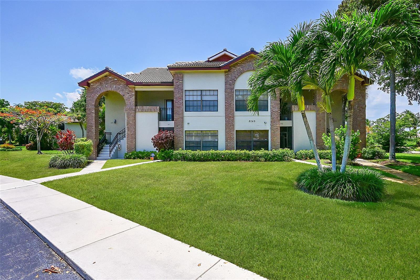 A two-story apartment building features brick accents, arched entryways, and a manicured front lawn — 8049 Aberdeen Drive # 101, Boynton Beach FL 33472, BOYNTON BEACH, FL
