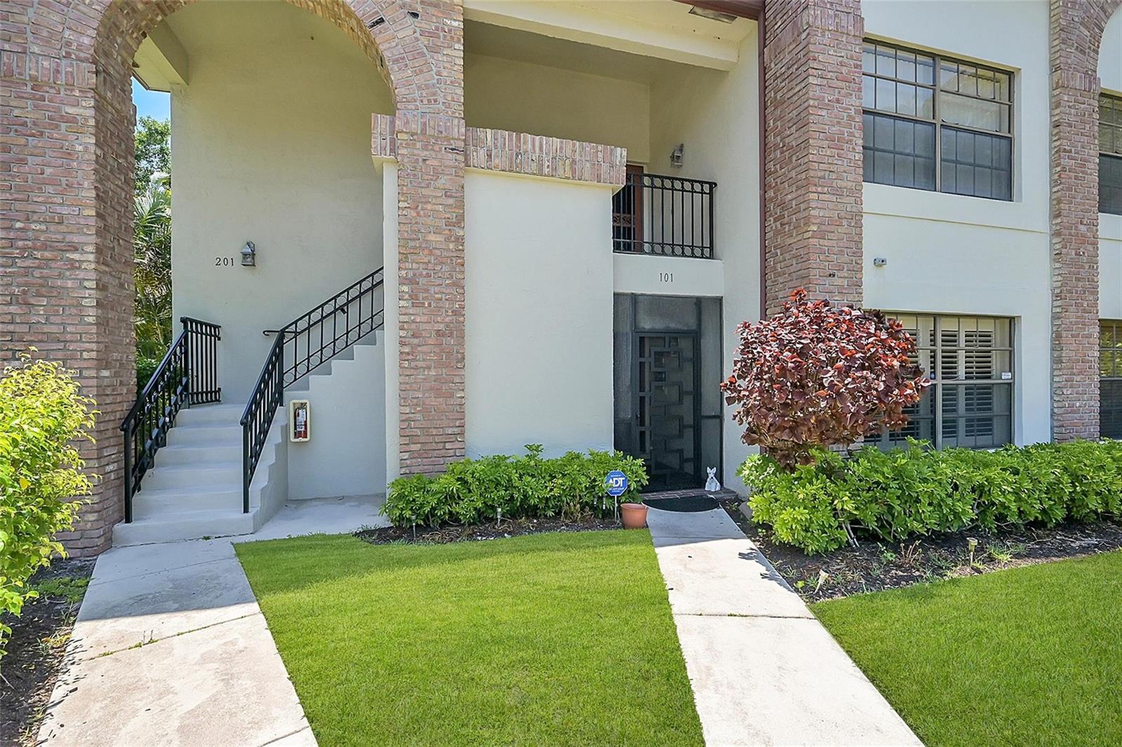 An exterior view of a two-story building featuring brick accents, stairs, and two unit entrances — 8049 Aberdeen Drive # 101, Boynton Beach FL 33472, BOYNTON BEACH, FL