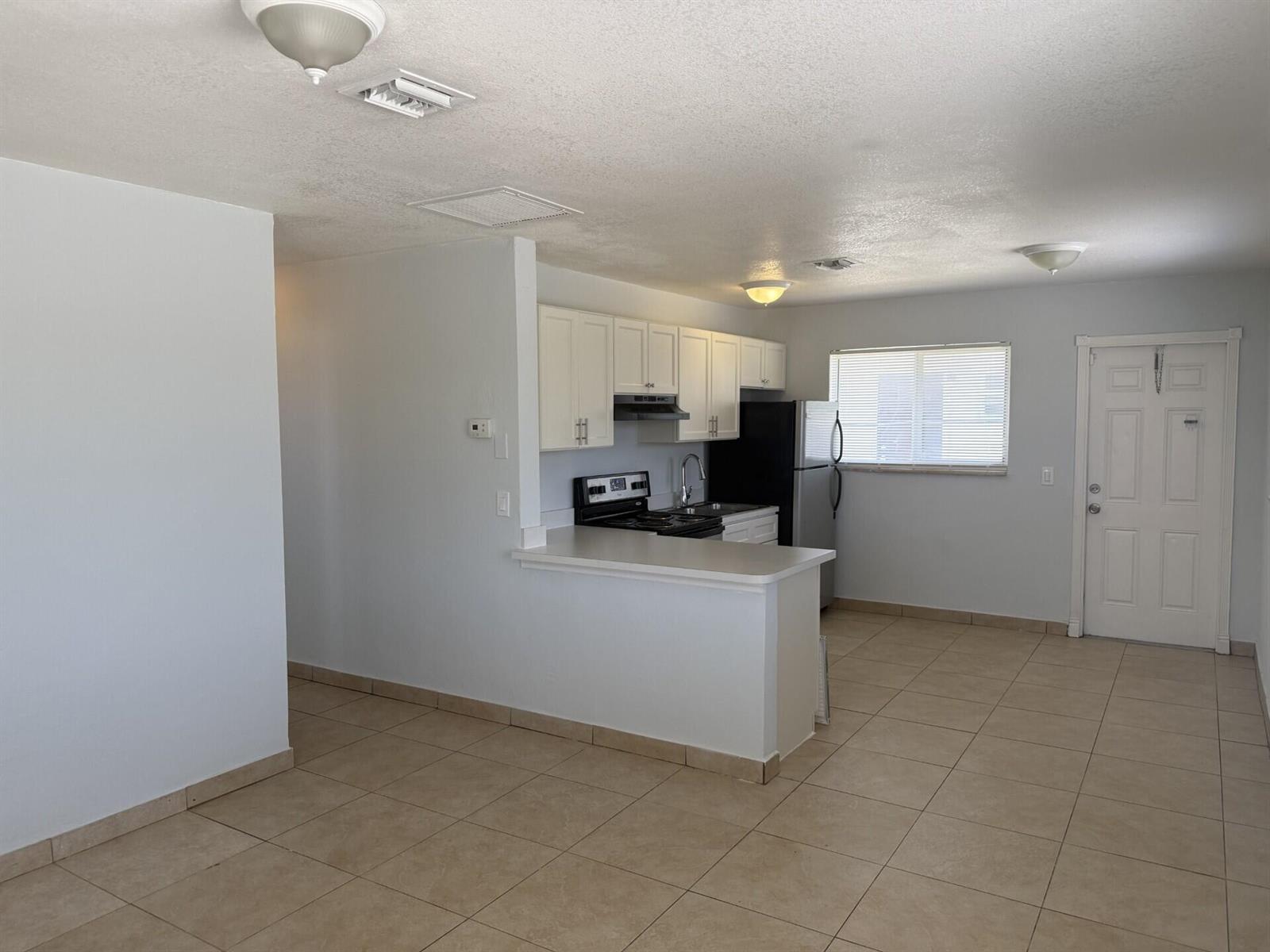 An open-concept kitchen features white cabinets, a breakfast bar, and light-colored tile flooring — 2820 Avenue S # 12, Riviera Beach FL 33404, RIVIERA BEACH, FL
