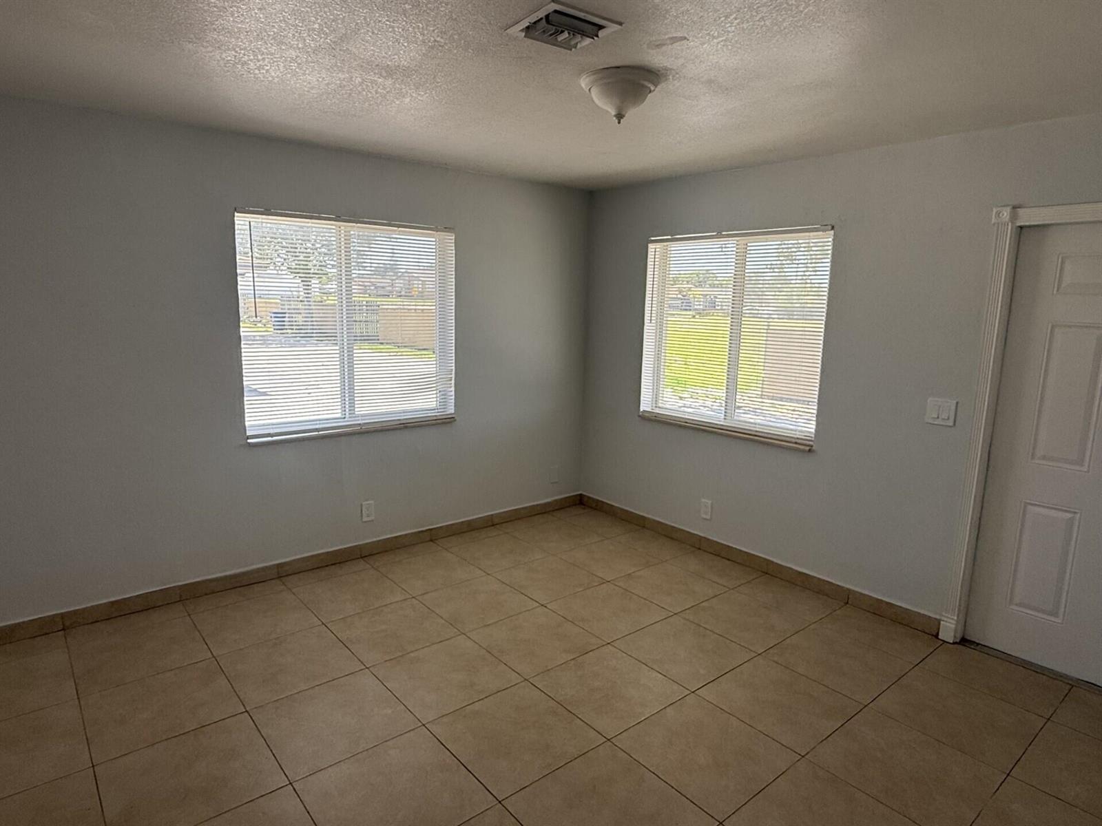 An empty room with light gray walls, tan tile flooring, two windows, and a door — 2820 Avenue S # 12, Riviera Beach FL 33404, RIVIERA BEACH, FL
