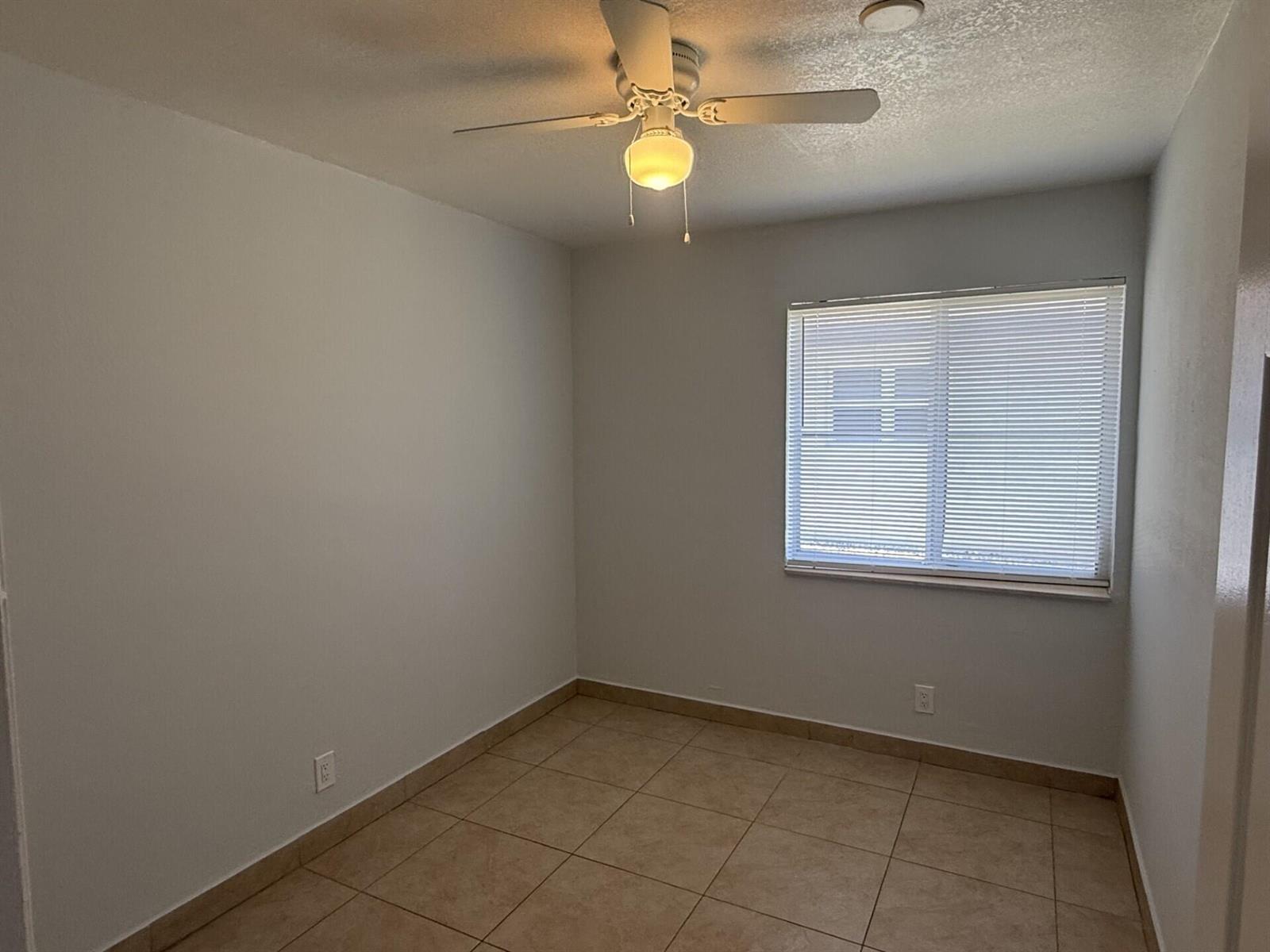 An empty room with light-colored walls, tile flooring, a ceiling fan, and a window — 2820 Avenue S # 12, Riviera Beach FL 33404, RIVIERA BEACH, FL