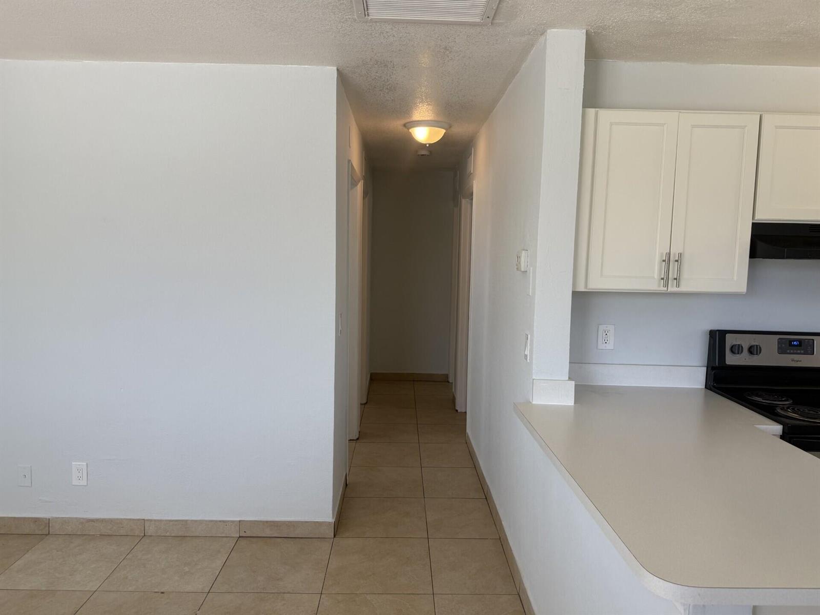 A hallway with tile flooring leads from a kitchen area toward a dimly lit corridor — 2820 Avenue S # 12, Riviera Beach FL 33404, RIVIERA BEACH, FL