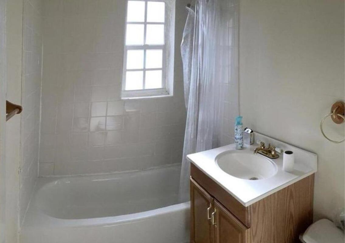 A bathroom with a white tiled bathtub, a window, and a wooden vanity with sink — 635 48th Street, West Palm Beach FL 33407, WEST PALM BEACH, FL