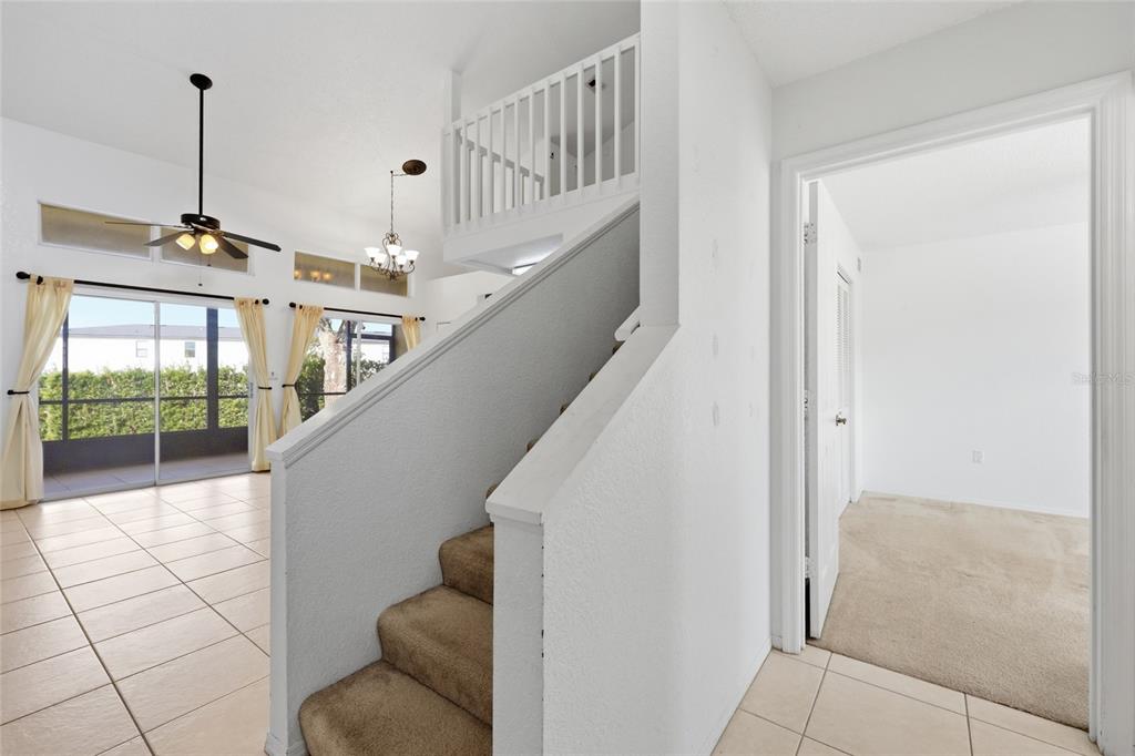 A staircase with tan carpet leads to a loft overlooking a tiled living area — 3176 TAMARIND CIRCLE UNIT 19, KISSIMMEE, FL