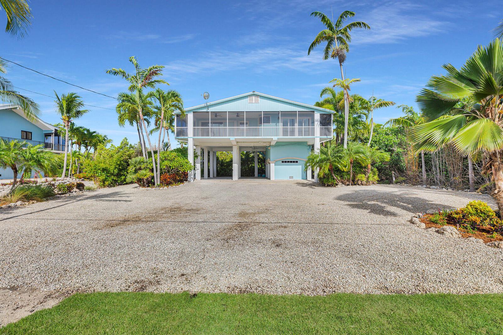 A light blue stilt house with a screened porch sits above a gravel driveway and palms — 1514 Shaw Drive, Key Largo FL 33037, KEY LARGO, FL