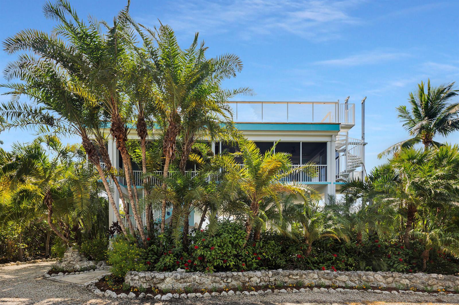A stilt house with a rooftop deck, spiral staircase, and lush tropical landscaping in front — 1514 Shaw Drive, Key Largo FL 33037, KEY LARGO, FL