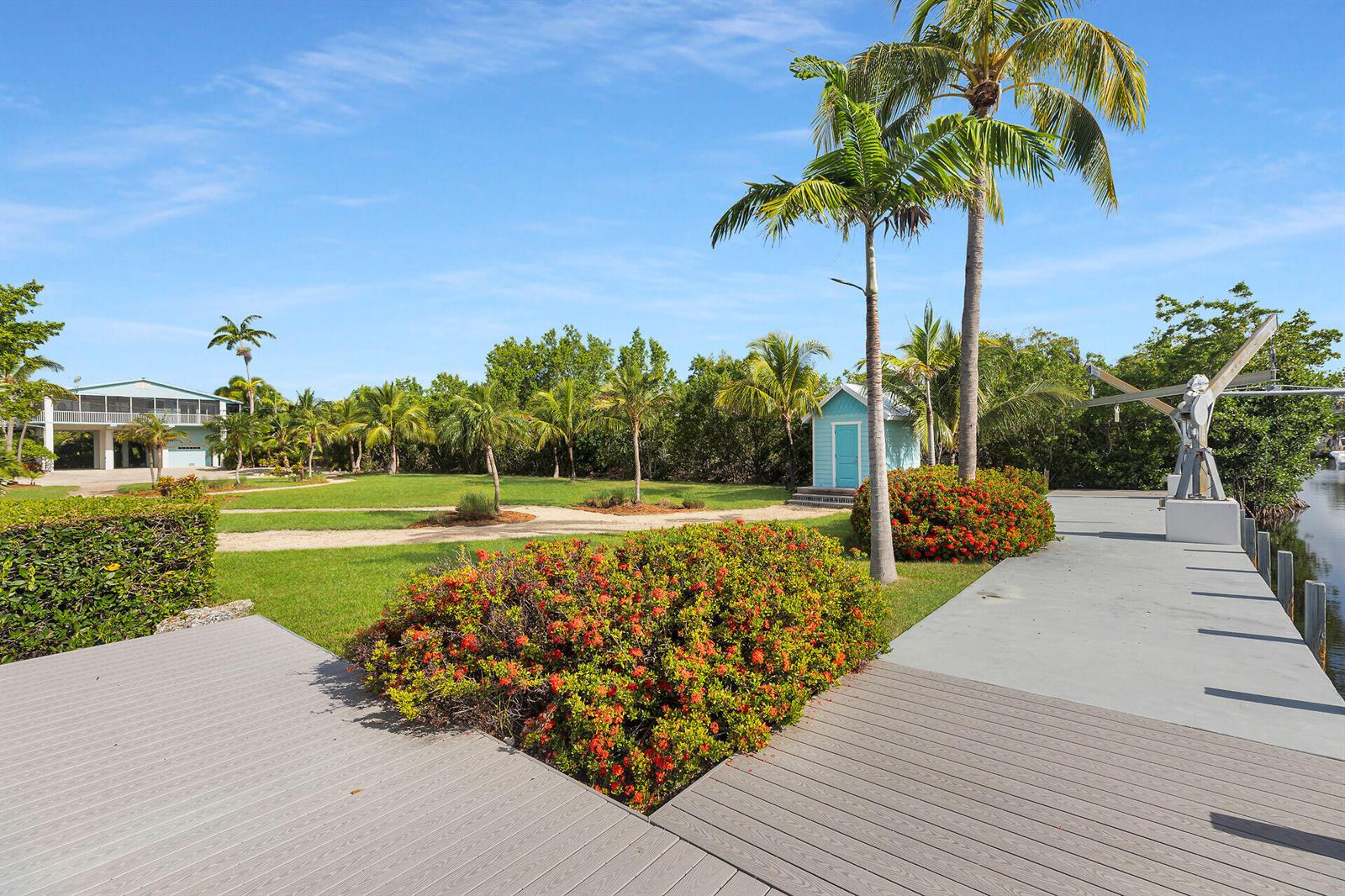 A grassy yard with palm trees, a small shed, and a wooden dock by water — 1514 Shaw Drive, Key Largo FL 33037, KEY LARGO, FL