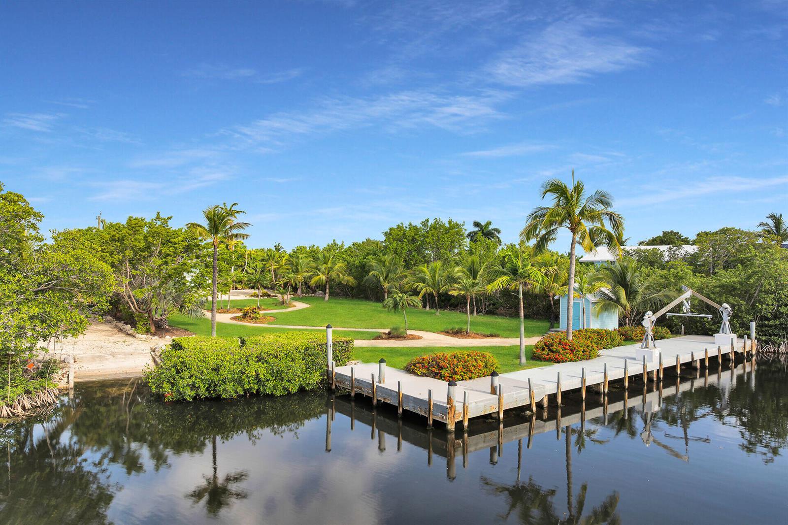 A wooden dock extends into a calm canal beside a grassy lawn with palm trees — 1514 Shaw Drive, Key Largo FL 33037, KEY LARGO, FL