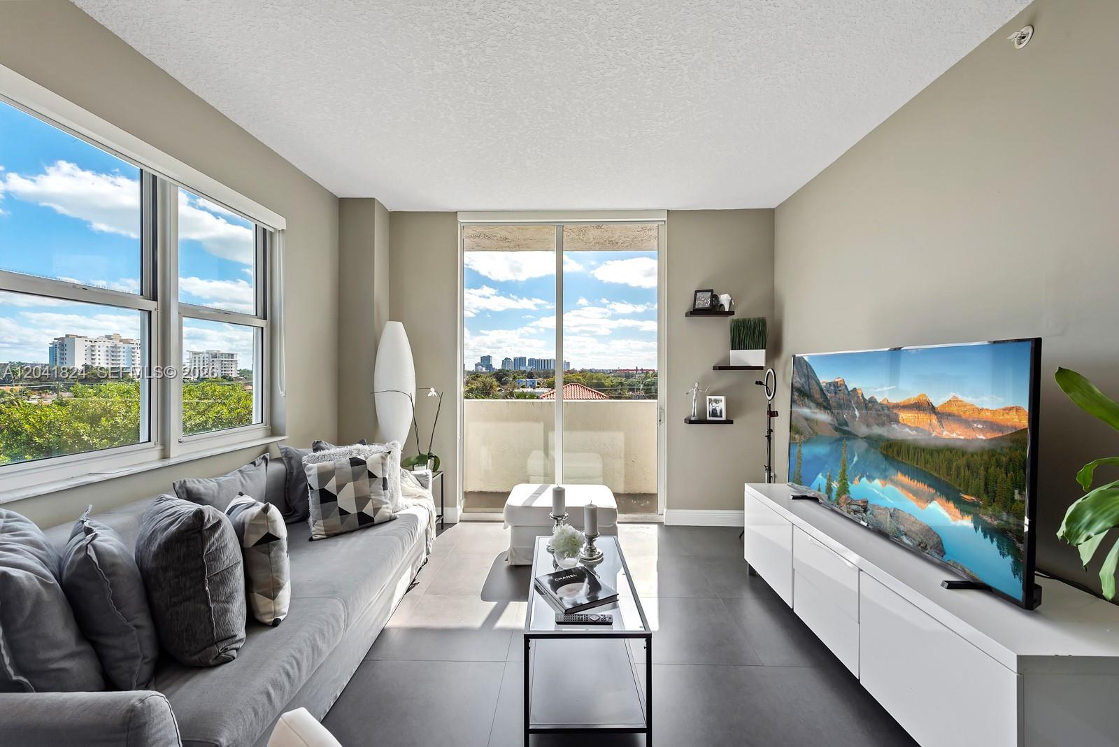 A modern living room features a gray sofa, a glass coffee table, and a television — 3000 CORAL WAY # 416, Miami FL 33145, MIAMI, FL